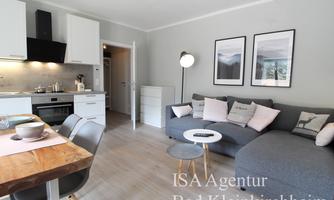 A modern apartment with an open kitchen and a cozy living room. The space is bright and inviting, with a gray sofa and a dining table.