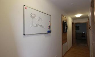 A bright hallway with a heart and the inscription "Welcome" on a sign. The floor is made of wood and the walls are in neutral colors.