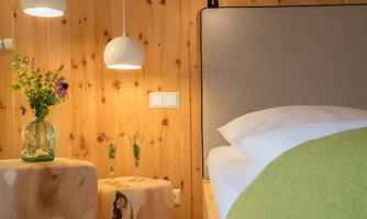 A cozy bedroom with wooden paneling and soft lighting. On a table, there are flowers and glasses, while the bed looks inviting.