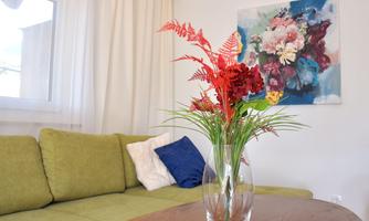 A cozy living room with a green couch and a wooden table. On the table, there is a vase with colorful flowers.
