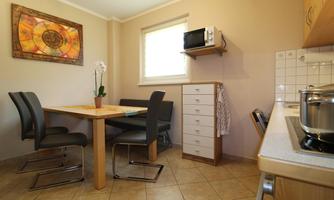 A bright kitchen with a wooden table and black chairs. In the background, there is a refrigerator and a microwave.