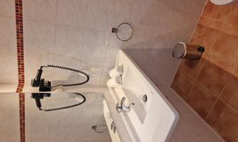 A modern bathroom with a sink, a mirror, and a towel. The floor is tiled and there is a metal trash can.