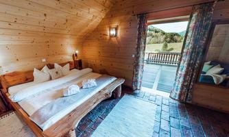 A cozy bedroom with wooden panels and a large bed. The terrace offers a beautiful view of nature.