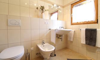 A modern bathroom with bright tiles and a large window. It includes a toilet, a bidet, and towels.