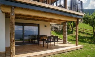 A cozy terrace with a wooden floor and modern furniture. In the background, gentle hills and a clear sky can be seen.
