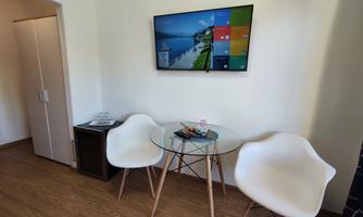 A cozy living area with a round table and two chairs. A television hangs on the wall, displaying a beautiful landscape.
