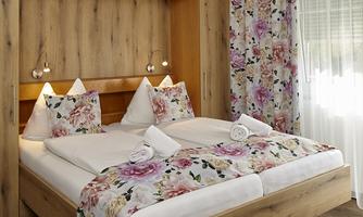 A cozy bedroom with a large double bed and floral pillows. The walls are decorated with colorful stripes and flower patterns.