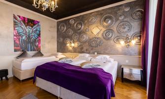 A modern bedroom with a large bed and a purple throw. An artistic painting of a butterfly hangs on the wall, and the lighting creates an inviting atmosphere.
