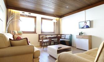 A modern living room with beige sofas and a wooden table. Large windows provide plenty of daylight and a pleasant atmosphere.