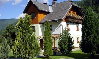 A beautiful house surrounded by green trees and shrubs. In the background, gentle hills can be seen.