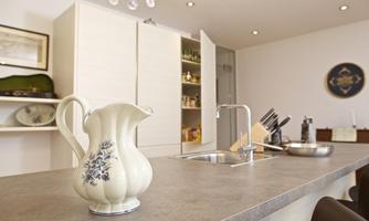 A modern kitchen with a bright color palette and an elegant kitchen island. A decorative kettle is on the countertop.