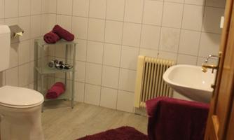 A modern bathroom with white tiles and a window. There is a toilet, a sink, and towels in purple color.