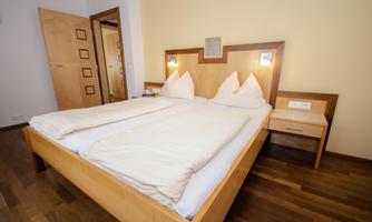 An inviting bedroom with a double bed and bright wood details. The walls are in soft colors and there is a nightstand next to the bed.