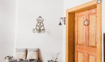 An inviting entrance area with a wooden door and decorative elements. On the side lie firewood and cushions for sitting.