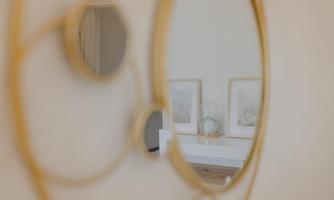 An elegant round mirror with a golden frame. Framed pictures and a decorative clock can be seen in the background.