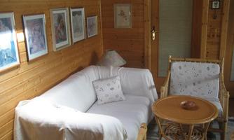 A cozy room with a white sofa and a round table. Various pictures hang on the walls, and there is a rattan armchair.