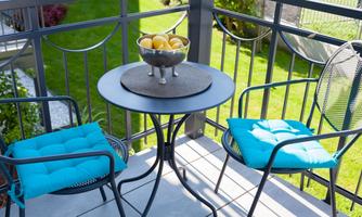 A cozy balcony with two chairs and a small table. On the table is a bowl of yellow apples.