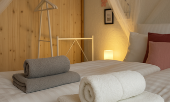A cozy bedroom with a bed and fresh towels. The warm tones and soft lighting create an inviting atmosphere.