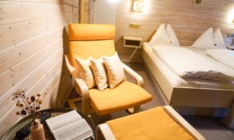 A cozy room with wooden walls and an orange armchair. Next to the armchair is a table with a book and a vase.