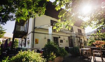 A cozy restaurant surrounded by trees and plants. The sun is shining, creating an inviting atmosphere.
