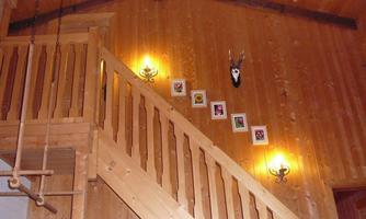 A wooden staircase leads to an upper floor in a cozy room. Picture frames hang on the wall, and there are wall lamps that create a warm atmosphere.