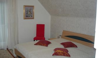 A cozy bedroom with a large bed and colorful pillows. There is a red chair and a window with curtains.