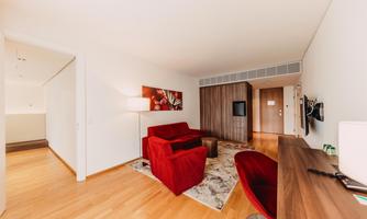 A modern living space with red sofas and a wooden desk. The room has bright walls and a large entrance.