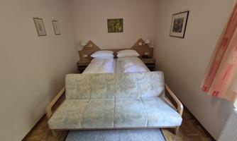 A simple bedroom with two beds and a sofa. The walls are bright and decorated with pictures.