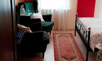 Double room “English Rose” with wooden floor, double bed, green armchairs, red infrared wall heater and window with daylight.