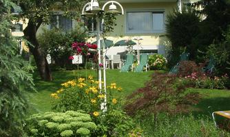 A beautiful garden with colorful flowers and a well-maintained lawn. In the background, cozy seating areas and a house can be seen.