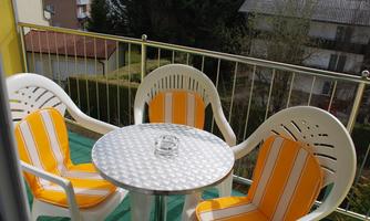 A small balcony with two white chairs and a round table. The chairs have yellow-striped cushions and there is an ashtray on the table.