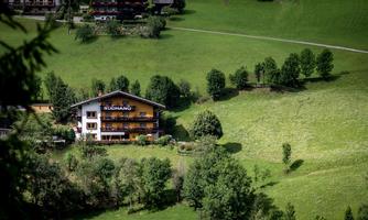 A picturesque house amidst a green landscape. The surroundings are hilly with many trees.