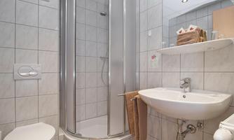 A modern bathroom with a shower, sink, and toilet. It is bright and clean with white tiles.