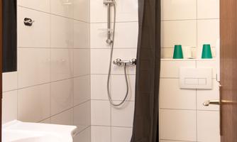 A modern bathroom with a shower and a surrounding shower partition. The walls are tiled with white tiles, and there is a sink as well as a toilet.