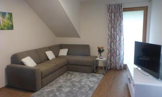 cozy modern living corner with a sofa and two cushions. On the table is a flower vase and a large flat-screen television is mounted on the wall.