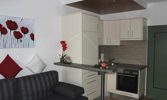 A modern kitchen with bright cabinets and an elegant living area. The room is decorated with red flowers and comfortable furniture.