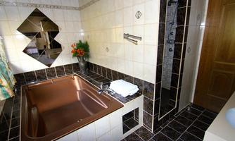 A modern bathroom with a brown bathtub and a glass shower. The walls are tiled and adorned with decorative elements.