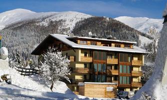 A modern house in a snow-covered landscape. In the background, there are tall mountains and a blue sky.