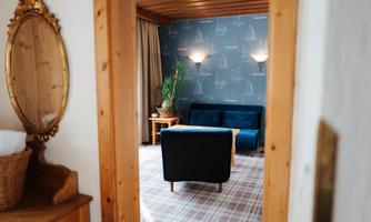 A cozy room with a blue sofa and a plant mat. Walls with maritime motifs and soft light create an inviting atmosphere.