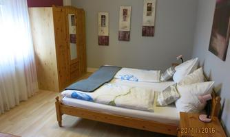 A cozy bedroom with two beds and white pillows. There is a wooden wardrobe and decorative pictures on the wall.