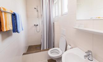 A modern bathroom with a shower and a toilet. There are colorful towels and a large window that lets in natural light.