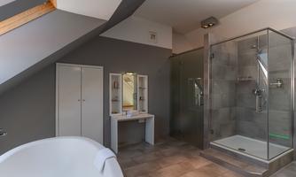 A modern bathroom with a glass shower and a freestanding bathtub. Light gray tiles and stylish furnishings create an elegant atmosphere.