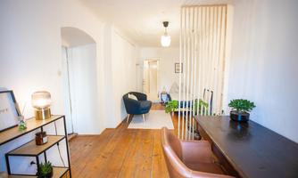 A modern living room with wooden flooring and a bright, friendly atmosphere. There is a partition wall, a desk, and comfortable seating.