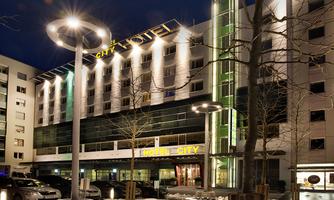 A modern hotel building with an illuminated facade at night. The surroundings are covered in snow, and there are street lamps as well as trees.