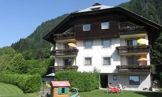 A cozy building with balconies and colorful sunshades. In the foreground, there is a small playground and green meadows.