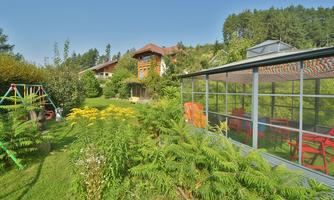 A beautiful garden with lots of green grass, colorful flowers, and a greenhouse. In the background, you can see a cozy house and a swing.