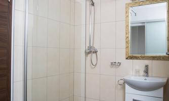 A modern bathroom with a glass shower and a small sink. The walls are brightly tiled and there is a mirror above the sink.