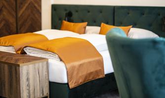 A stylish bedroom with a large bed and golden blankets. Next to the bed is a wood-colored nightstand.
