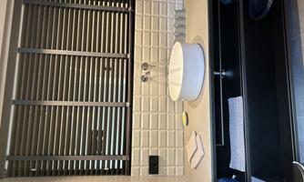 A modern bathroom with a round sink bowl on a light countertop. The walls are covered with white tiles, and there are vertical blinds for light control.