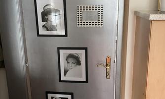 A silver door with three framed black-and-white photos. Next to the door is a light-colored piece of furniture.